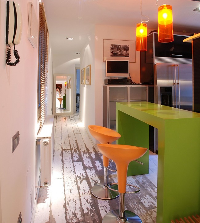 Oranžové židle ve společnosti s oranžovými lampami a zeleným stolem dodávají běžné kuchyni šťavnatost a nudu.
