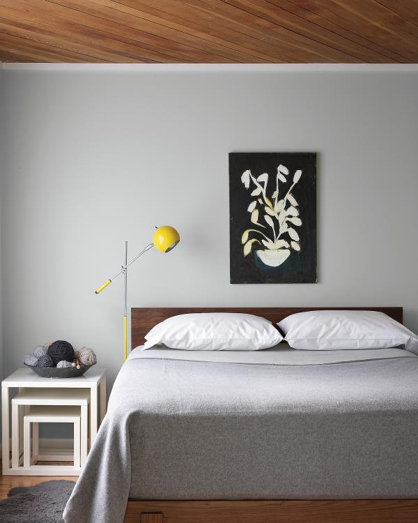 Aktualna kolorystyka ścian szary sypialnia jasnoszary na ścianie narzuta białe poduszki małe podświetlenie w żółtej lampce