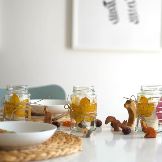 Décorez la salle à manger avec une décoration automnale La table à manger est décorée de petites figurines en bois à côté de pots à feuilles jaunes