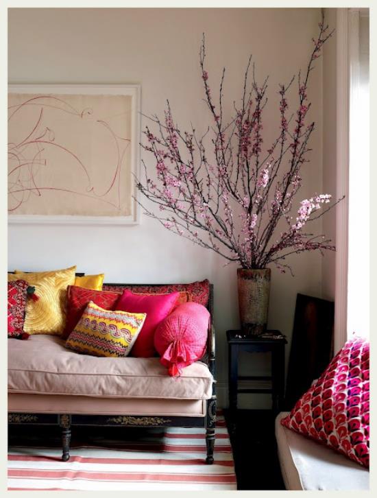 Wiosenna dekoracja z kwiatami wiśni duży wazon ładnie ułożone gałązki wiśni w rogu salonu sofa kolorowe rzucanie poduszkami