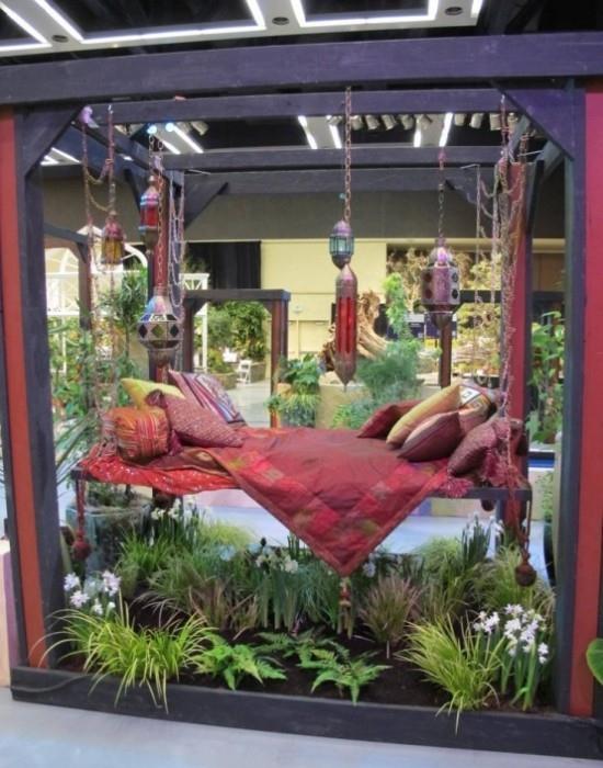 Wiszące łóżko na tarasie w stylu boho kolorowo udekorowane w otoczeniu zielonych roślin