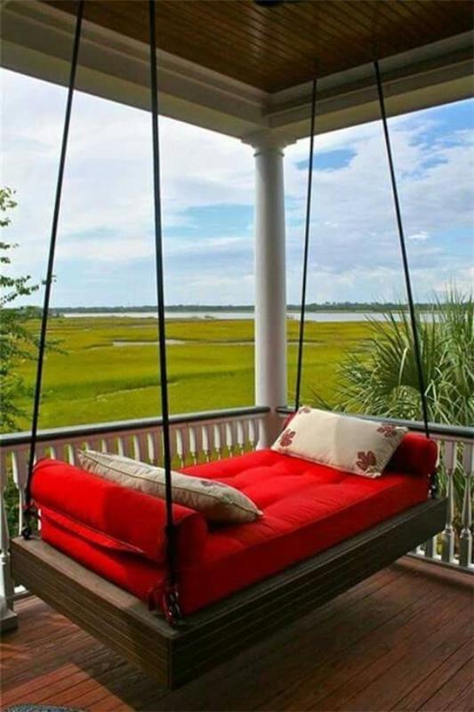 Łóżko wiszące na zewnątrz na zadaszonym tarasie, czerwona tapicerka, dwie ozdobne poduszki, wspaniały panoramiczny widok na zielony krajobraz