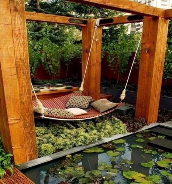 Łóżko wiszące na zewnątrz nietypowy design w stylu japońskim tuż nad stawem, wiele zielonych roślin ozdobnych poduszek