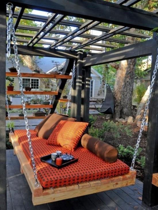 Łóżko wiszące na zewnątrz w ogrodzie tapicerka w kolorze pomarańczowym taca z filiżankami kawy świeca