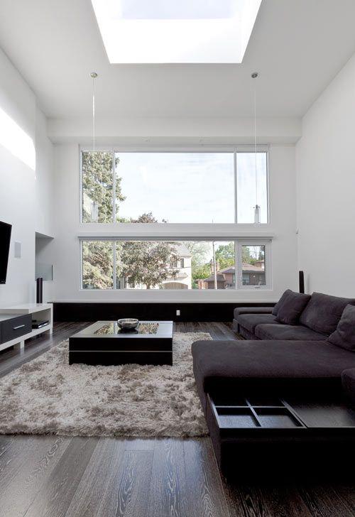 Minimalizm w salonie idealny projekt ciemna sofa narożna dywan TV ściana duże okno dużo naturalnego światła