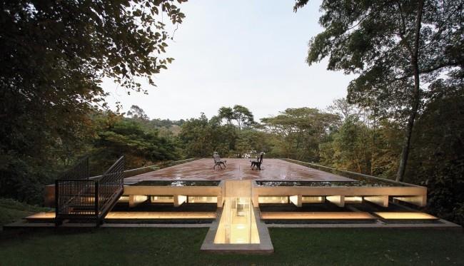 Maison moderne en verre et béton dans la forêt tropicale, large toit-terrasse recouvert de planches de bois résistantes aux intempéries