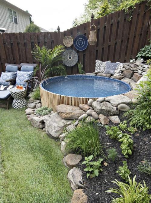 Okrągłe baseny ogrodowe na podwórku ozdobnie wyłożone kamiennym ogrodzeniem, obok niego drewniana część wypoczynkowa