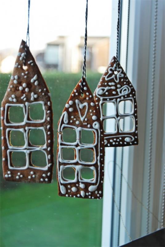 Świąteczna dekoracja okienna, trzy domowe domki z piernika zawieszone na oknie