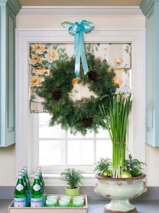 Świąteczna dekoracja okna duży wieniec z zielonych szyszek i niebieskiej wstążki na oknie kuchennym