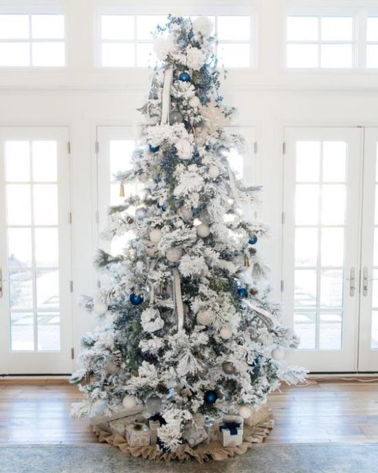 Décorez le sapin de Noël en blanc et argent devant la fenêtre, placez quelques boules bleues brillantes comme accents