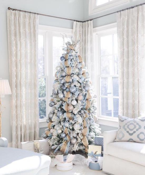 Sapin de Noël décoré dans une ambiance blanche et argentée décorée de cadeaux accrocheurs de sapin de Noël en dessous