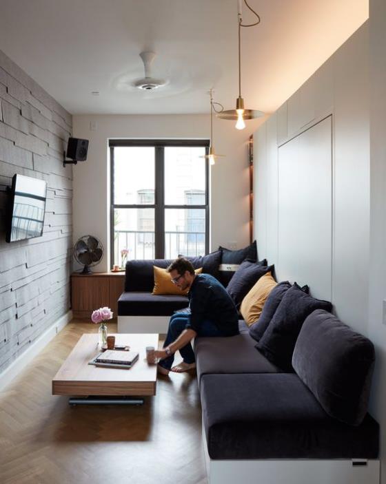 Design d'intérieur contemporain, salon moderne et étroit, canapé d'angle violet foncé, TV sur le mur de briques