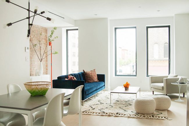 Tmavě tyrkysová sedačka vypadá ve světlém interiéru obývacího pokoje ve skandinávském stylu co možná nejvíce luxusně a akcentovaně