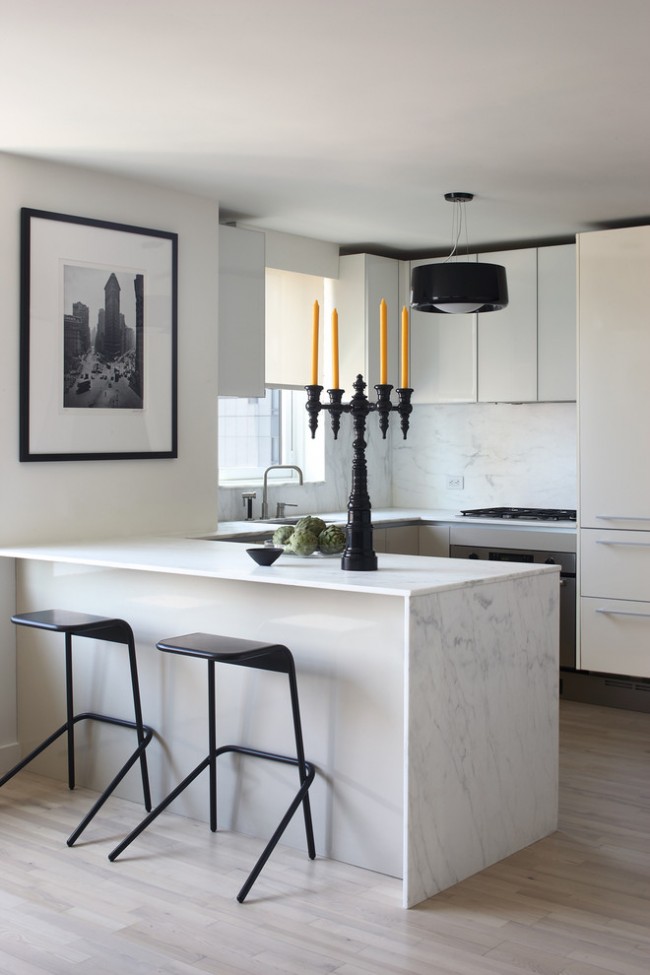 Moderní kuchyně s převahou bílé, zředěné černými prvky. Obraz doplňují žíly z mramoru a černobílé fotografie.