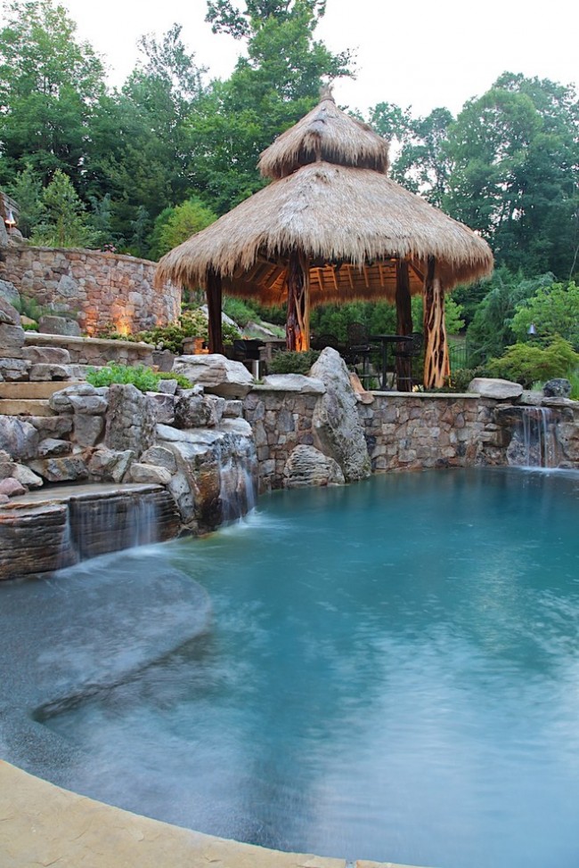 Ein grob gearbeiteter Pavillon im tropischen Stil mit künstlichem Teich mit kleinen Wasserfällen im rustikalen Stil vor der Kulisse eines künstlichen Teichs mit kleinen Wasserfällen