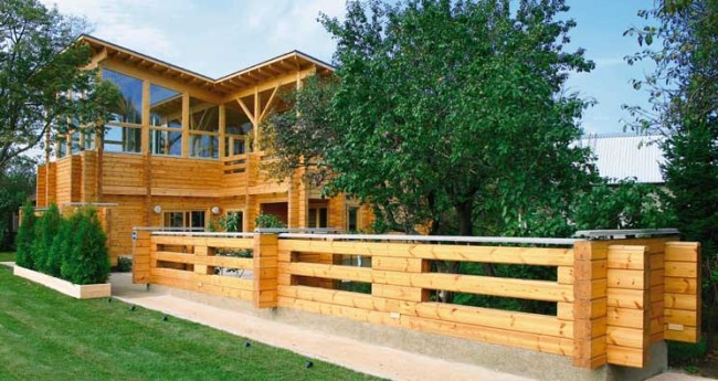 Dřevěné domy z profilovaného dřeva. Ukázka funkční výzdoby pozemku s dřevěnou tyčí, ze které je postaven dům