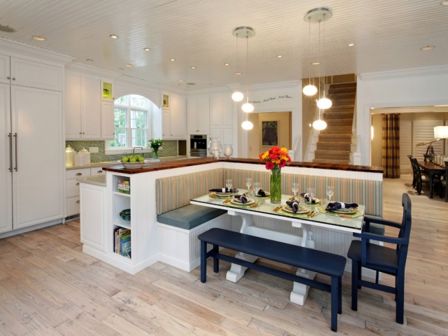 Prostorná studiová kuchyň ve světlých barvách s akcenty přírodního dřeva a modrými prvky v jídelním nábytku