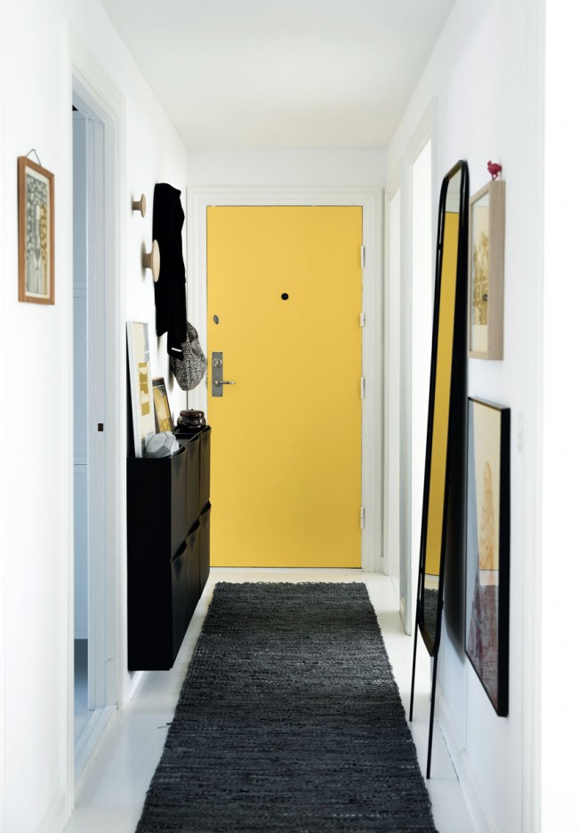 Тесен коридор с топъл акцент върху жълтите входни врати, високо огледало визуално увеличава пространството, а малък стенен шкаф практически държи обувки и всички необходими неща