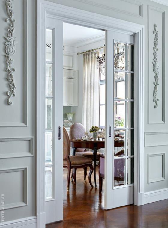 Francuskie drzwi balkonowe wysokie ościeżnice w kolorze jasnoszarym pasują do klasycznego wystroju pomieszczenia i prowadzą do jadalni