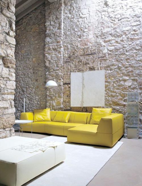 canapé en cuir jaune coussins murs en pierre brute tapis de table blanc