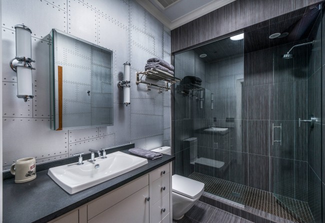 Ein sehr maskulines Design eines grauen Badezimmers, in dem übertriebene Strenge die Handlung in der Zeichnung einer Akzentwand zum Thema genietete Bleche negiert