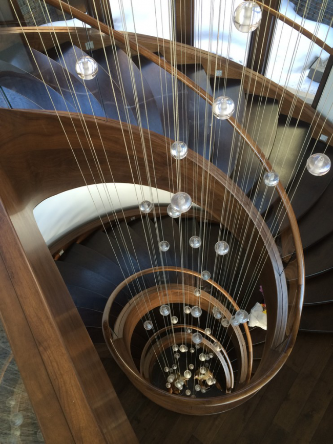 Eine Holzwendeltreppe kann mit einer Installation in Form von Zierfäden mit Perlen verziert werden, die über die gesamte Höhe der Treppe herabhängen
