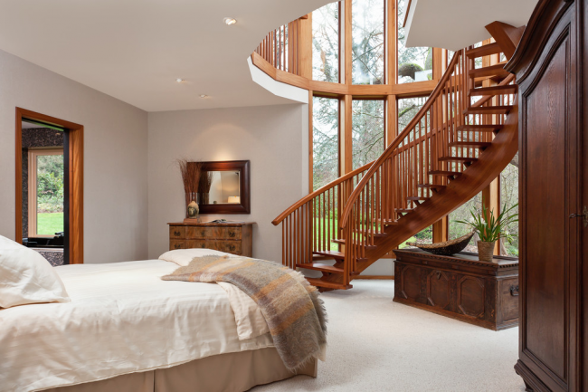 Eine Holztreppe in Verbindung mit einer Panoramaverglasung erweitert die Grenzen dieses Schlafzimmers optisch und macht es zum hellsten und luftigsten Raum