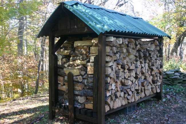 Ein sehr organisch aussehender Brennholzschuppen. Bitte beachten Sie, dass die gesamte Struktur auf kleinen Betonblöcken montiert ist, um einen Holz-Boden-Kontakt zu vermeiden