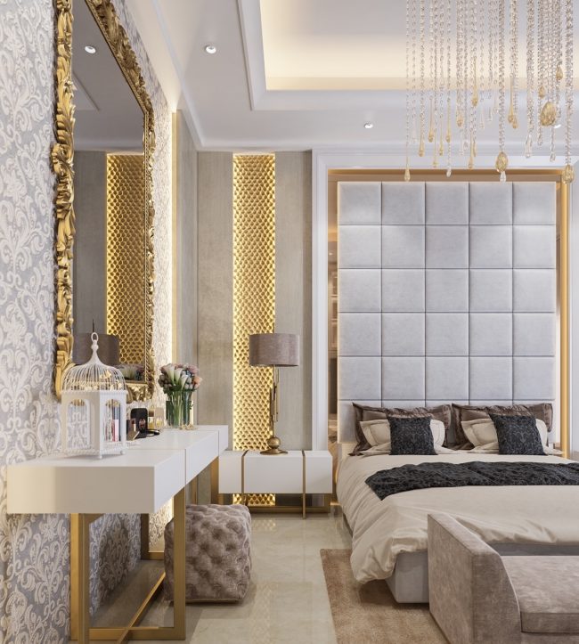 Ein luxuriöses Schlafzimmer mit einem Hauch von Dekadenz in der Einrichtung. Das hohe Kopfteil ist mit Wildlederimitat bezogen und der massive vergoldete Spiegelrahmen spiegelt die leuchtenden Goldakzente an der Wand wieder