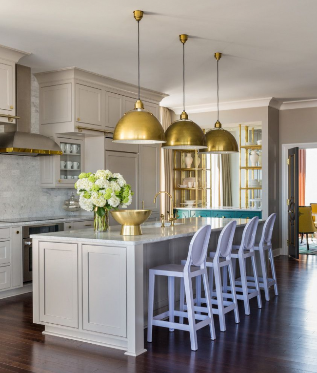 Teplá šedá v klasickém interiéru kuchyně. Zlaté dekorativní detaily: kuchyňské příslušenství, závěsná stínidla, kuchyňský faucet, otevřené police na nádobí atd.