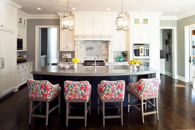 Кухненски остров от абанос с плотове от сив гранит и меки кресла в ярък абстрактен растителен принт е центърът на модерна кухня в сиво -бяла цветова схема