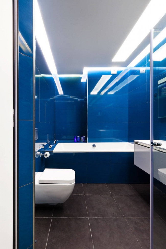حل جريء وملون للغاية: اللمعان الأزرق المتسع للبلاط والإضاءة الباردة في حمام صغير مشترك
