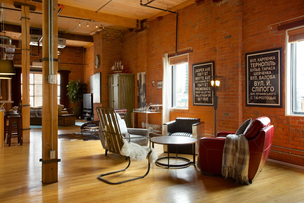 Ein modernes Apartment im Loft-Stil mit gemischter Beleuchtung, die die Bereiche des Raumes ohne Trennwände bestimmt. Ein runder Couchtisch, vier verschiedene Sessel und eine Stehlampe aus grobem Metall bilden eine Leseecke