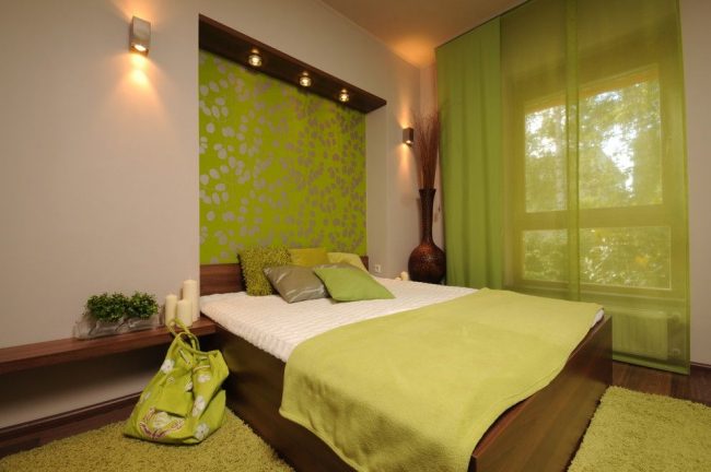 Tmavé dřevo ve výzdobě nábytku a podlahy, panel nad jablečně zelenou postelí, polštáře v různých odstínech zelené a další interiérové ​​prvky, které v interiéru zdůrazňují klasickou kombinaci zelené a hnědé