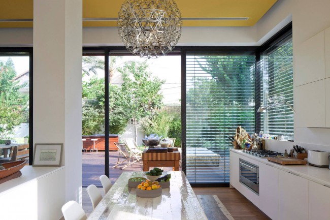 Neobvyklé žaluzie ve studiové kuchyni ve světlých barvách s akcenty na dřevěných interiérových prvcích a jasně žlutým stropem v soukromém domě